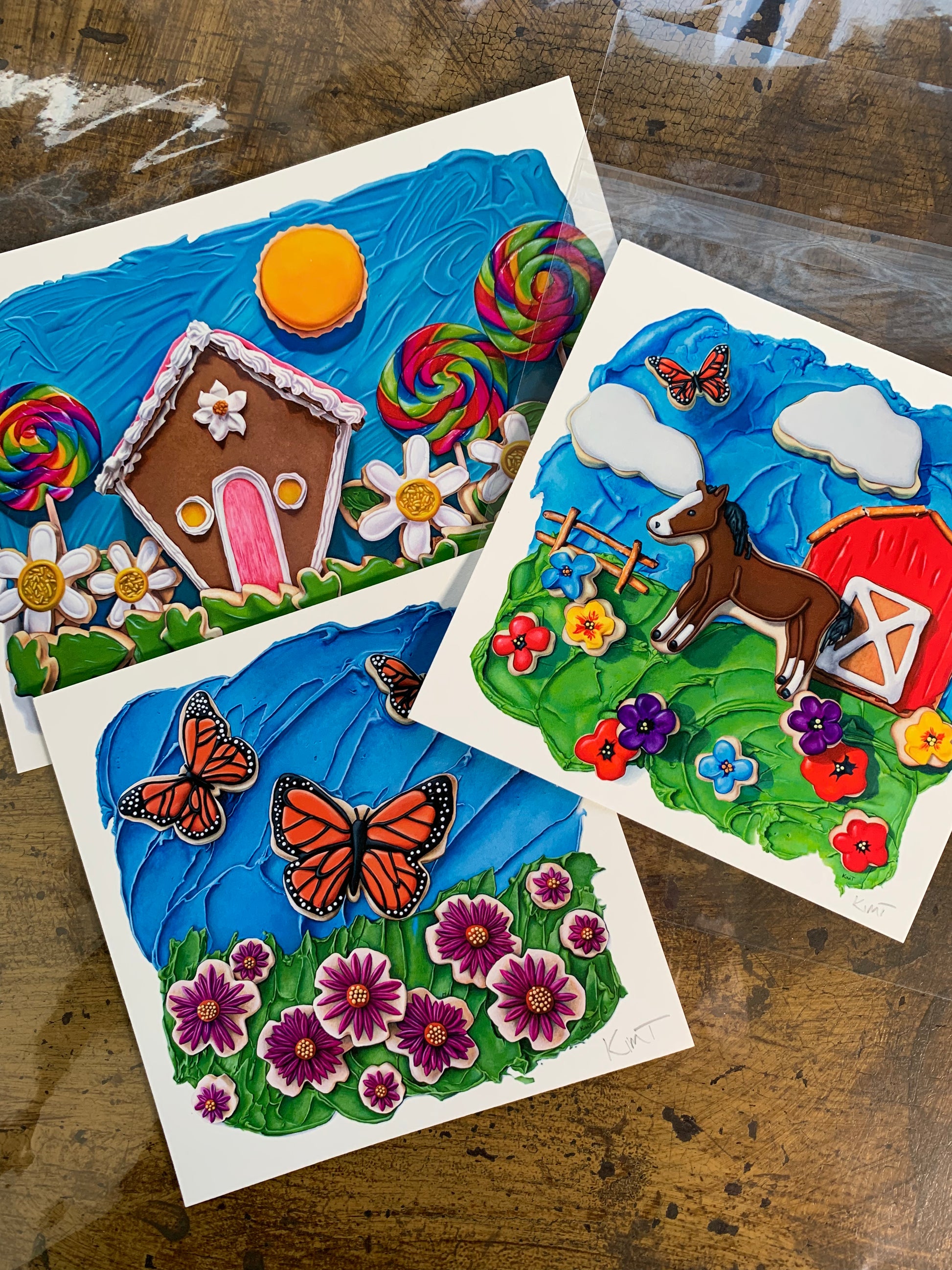 Three of the mini sweet escapes art print club art prints by Kim Testone, featuring trompe l'oeil cookie landscape paintings. 
