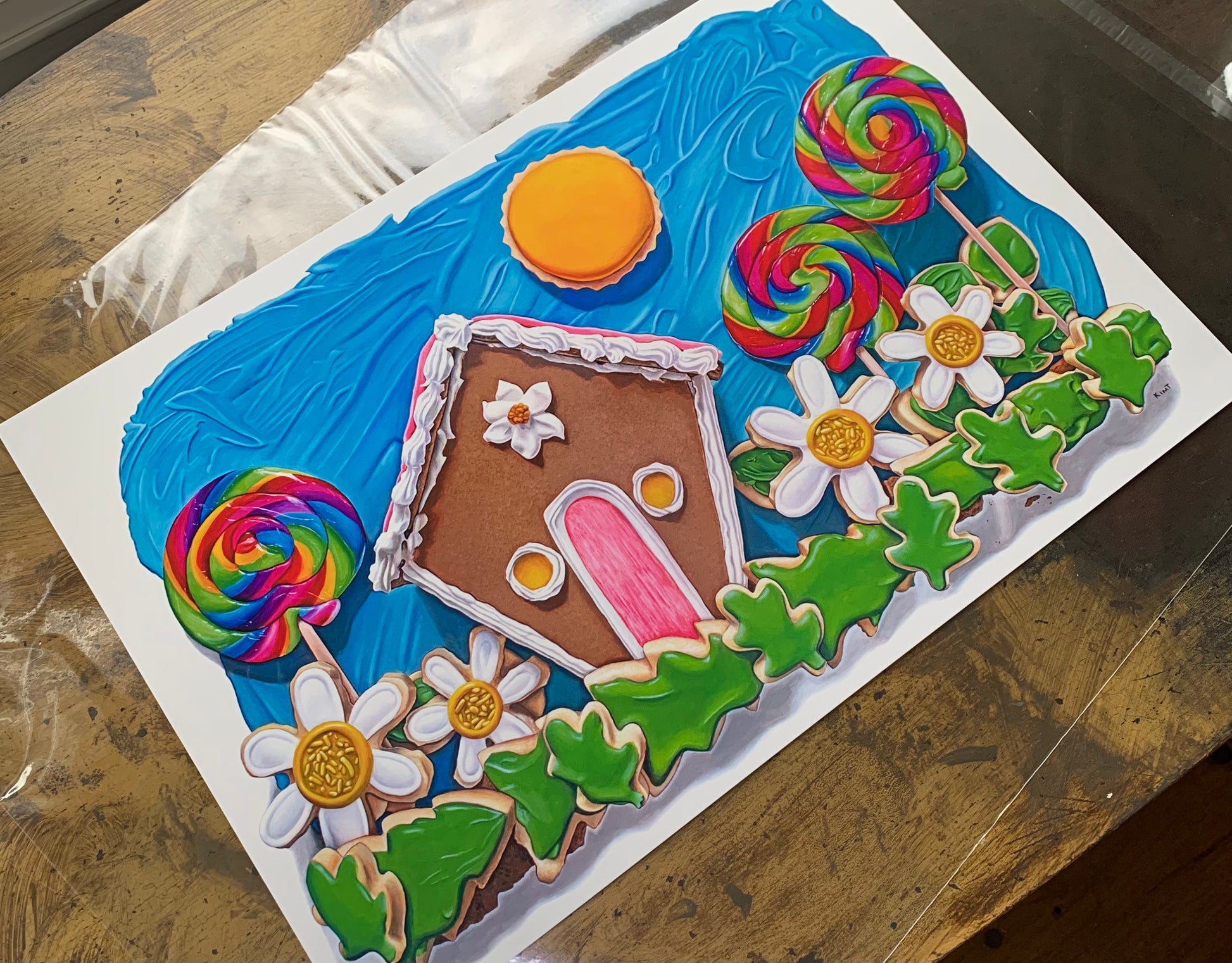 Here Comes the Sun art print by Kim Testone, based on an original trompe l'oeil painting of a gingerbread house with three swirly rainbow lollipops, a field of cookie flowers and cookie greenery, a cookie sun, set against a blue frosting sky.