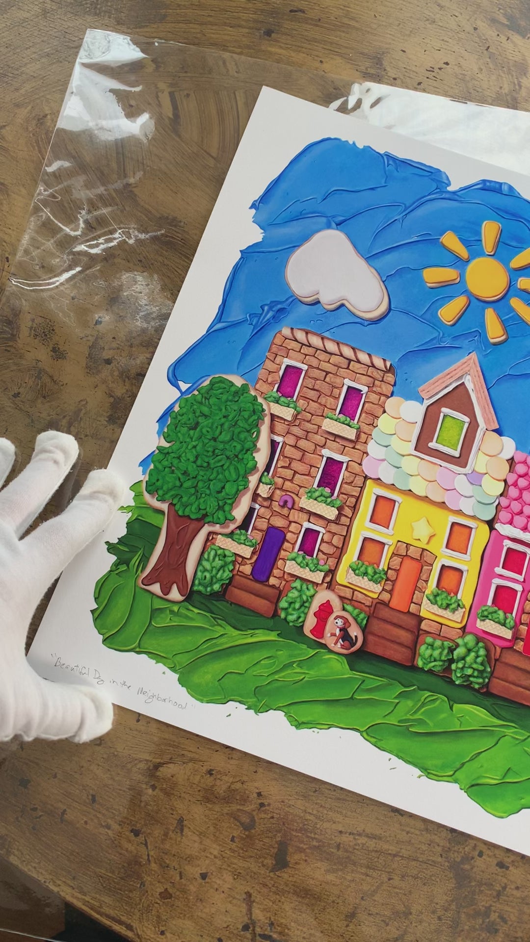 Video of the Beautiful Day in the Neighborhood art print by Kim Testone, based on an original painting that features a row of five gingerbread buildings with a blue frosting sky, cookie clouds and a cookie sun, with cookie and cereal trees and six cute animals, creating a whimsical gingerbread neighborhood.